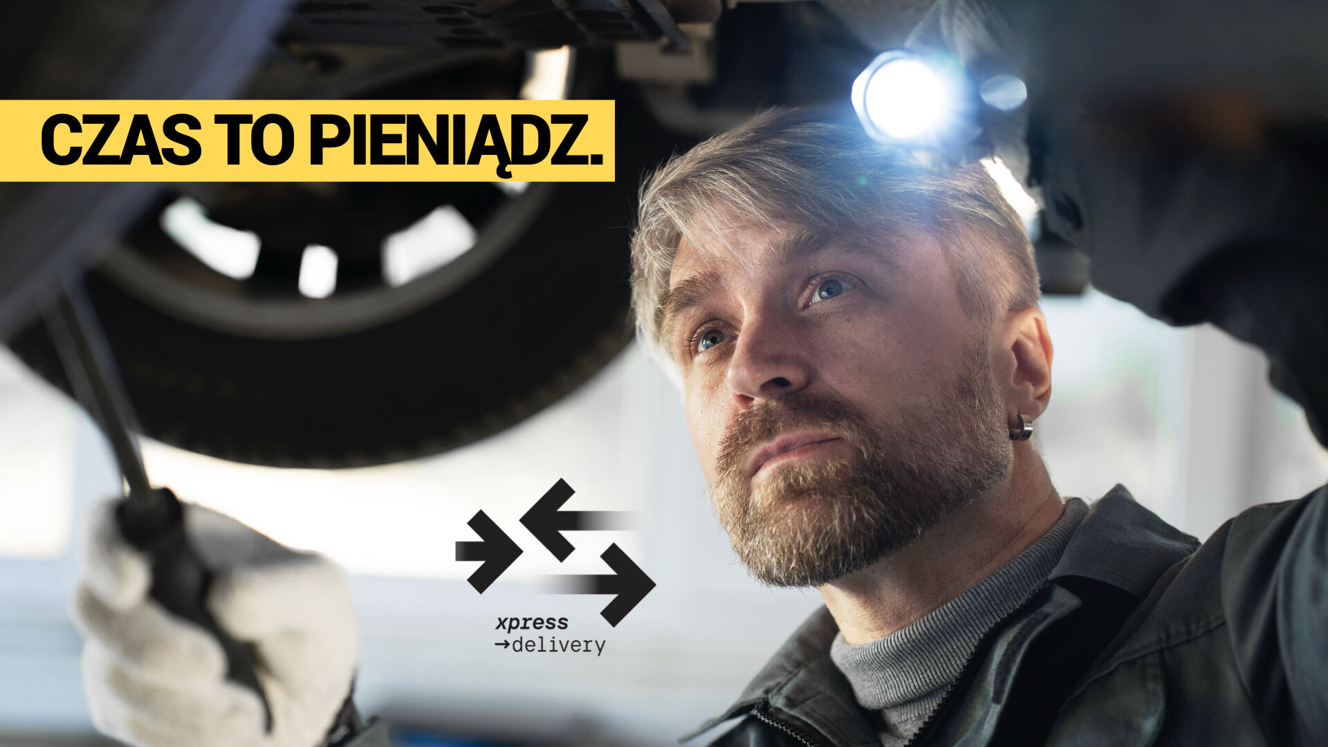 Mechanik samochodowy pracujący pod podnośnikiem – ekspresowa dostawa części do warsztatu dzięki Xpress Delivery. Hasło: „Czas to pieniądz”.